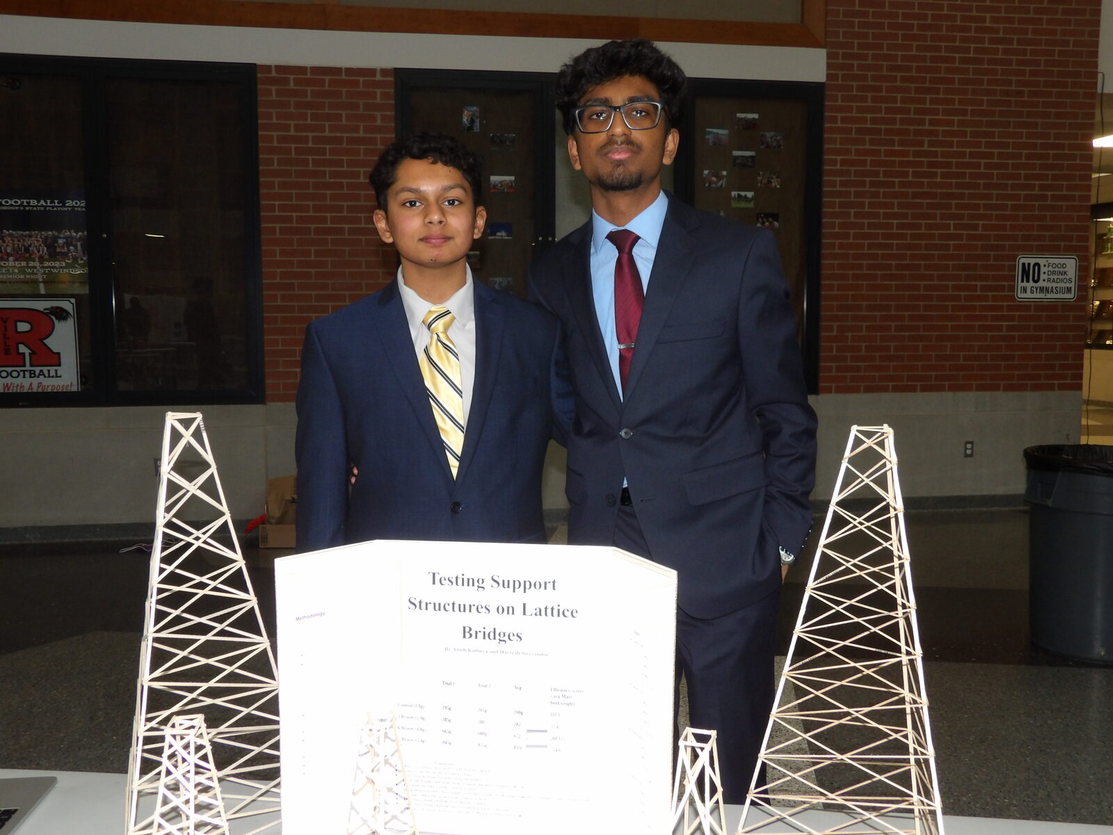 Two SciFest 2026 presenters with physical lattice bridge models supporting their board, Testing Support Structures on Lattice Bridges.